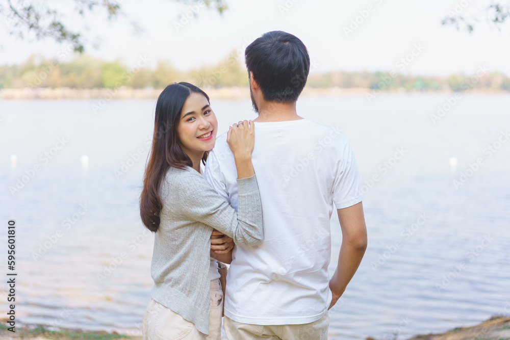 Young couple in love smiling and embracing while picnic and standing near lake in park