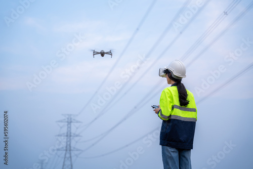 A female electrical engineer flying drone surveying area of high voltage pylons with wearing vr goggles in aerial view to inspect equipment on high voltage pylons.