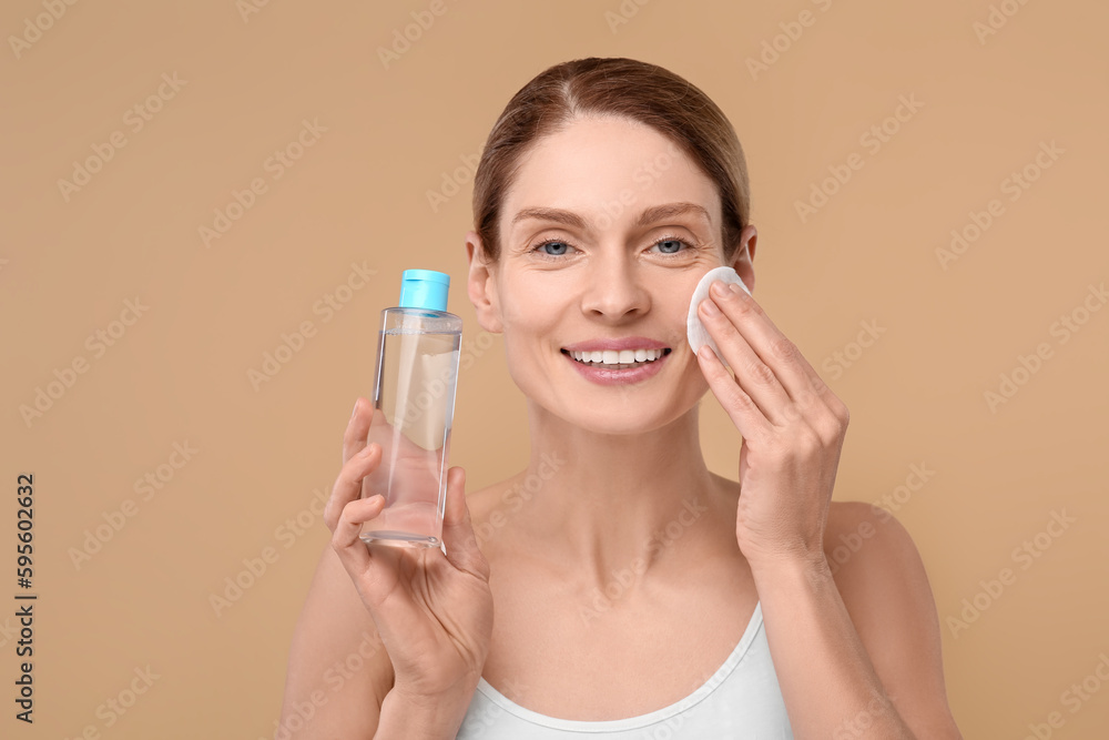 Beautiful woman removing makeup with cotton pad on beige background Beautiful woman removing makeup with cotton pad on beige background
