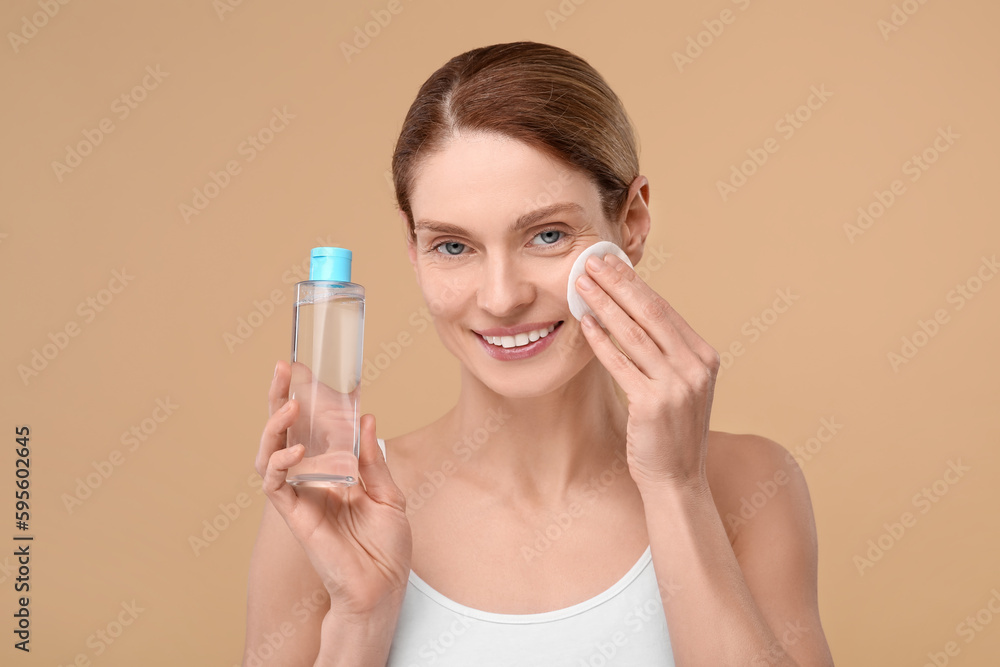 Beautiful woman removing makeup with cotton pad on beige background Beautiful woman removing makeup with cotton pad on beige background