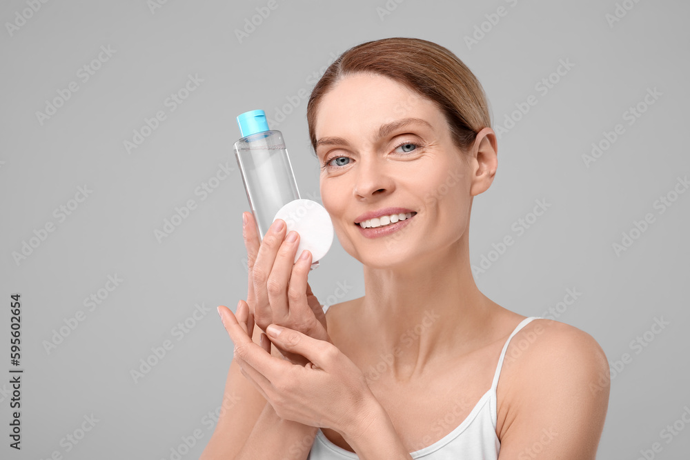 Beautiful woman with makeup remover and cotton pad on gray background, space for text Beautiful woman with makeup remover and cotton pad on gray background, space for text