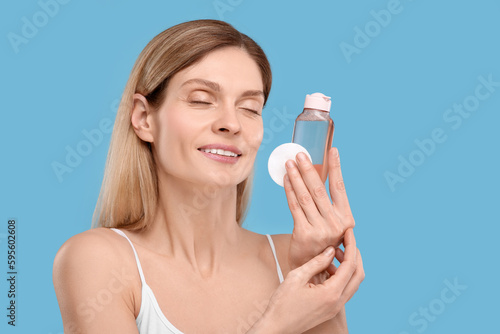 Beautiful woman with makeup remover and cotton pad on light blue background