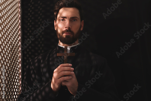 Catholic priest in cassock holding cross in confessional