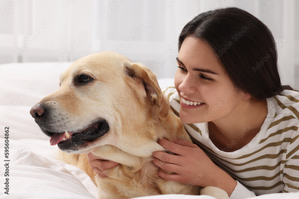 Happy woman with cute Labrador Retriever on bed at home Happy woman with cute Labrador Retriever on bed at home