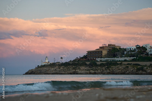 Fototapeta Naklejka Na Ścianę i Meble -  a lighthouse on the beach at dusk with a pink and white cloud in the sky