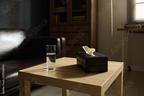 Small wooden square table with glass of pure water and black box containing tissues prepared for patients of psychotherapist © pressmaster