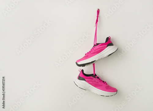 Pair of stylish pink sneakers hanging on white wall background. Fashionable stylish sport casual shoes. Modern creative minimalistic layout with footwear. Mock up for design advertising for shoe store