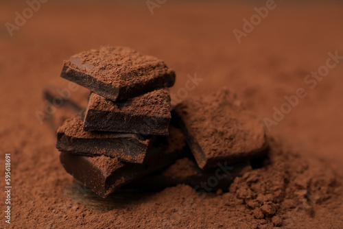 Pieces of tasty chocolate and cocoa powder on wooden table, closeup