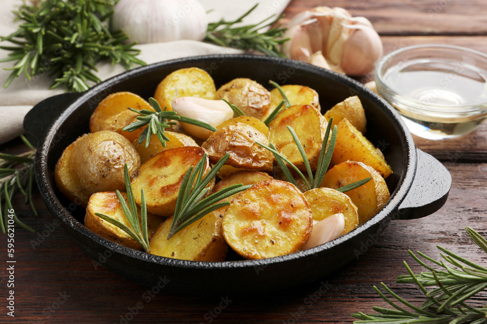 Delicious baked potatoes with rosemary in frying pan on wooden table, closeup Delicious baked potatoes with rosemary in frying pan on wooden table, closeup
