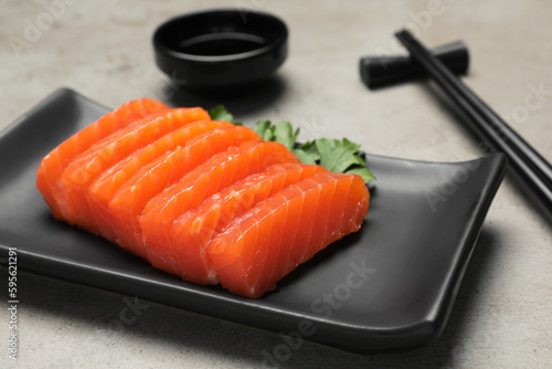 Plate of tasty salmon slices and parsley on grey table, closeup. Delicious sashimi dish