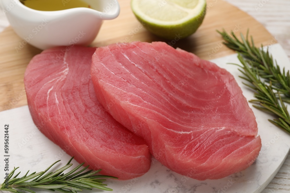 Fresh raw tuna fillets with rosemary, lime and oil on board, closeup Fresh raw tuna fillets with rosemary, lime and oil on board, closeup