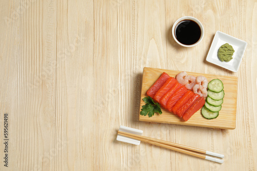 Delicious sashimi set of salmon and shrimps served with cucumbers, parsley, wasabi and soy sauce on wooden table, flat lay. Space for text
