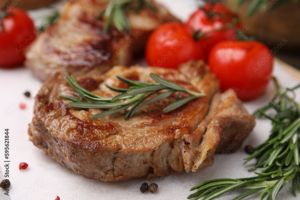 Delicious fried meat with rosemary, tomatoes and spices on white table, closeup Delicious fried meat with rosemary, tomatoes and spices on white table, closeup