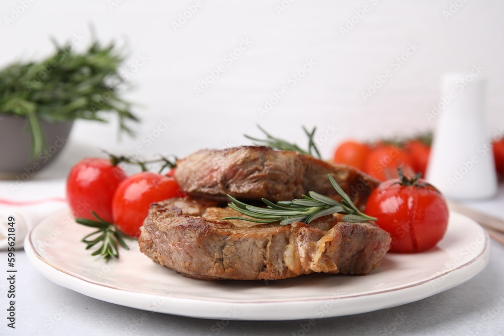 Delicious fried meat with rosemary and tomatoes on white table, closeup Delicious fried meat with rosemary and tomatoes on white table, closeup