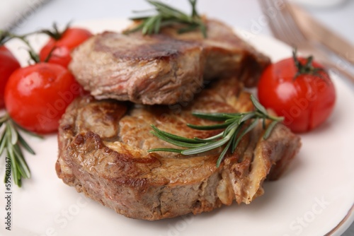 Delicious fried meat with rosemary and tomatoes on plate, closeup