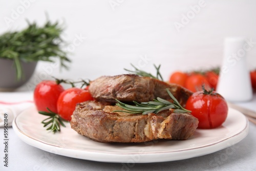 Delicious fried meat with rosemary and tomatoes on white table, closeup