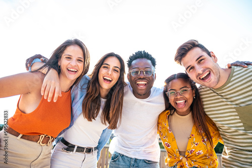 Low angle view of a happy group of multiracial friends looking at camera, enjoying outdoors. Multiethnic cheerful young people