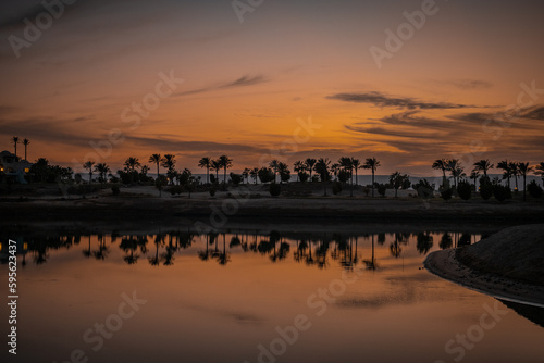 Sonnenuntergang an der Lagune bei Ancient Sands in El Gouna, Ägypten. Die LAndschaft mit den Plamen und Häusern spiegelt sich im Wasser.