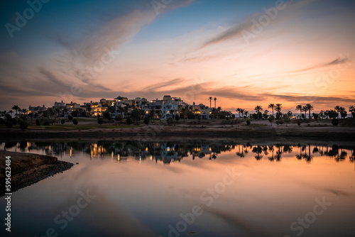 Sonnenuntergang an der Lagune bei Ancient Sands in El Gouna, Ägypten. Die LAndschaft mit den Plamen und Häusern spiegelt sich im Wasser.