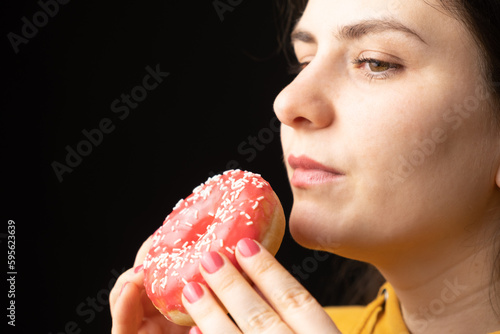 A woman bites a large red donut, a black background, a place for text. Gluttony, overeating and sugar addict. photo