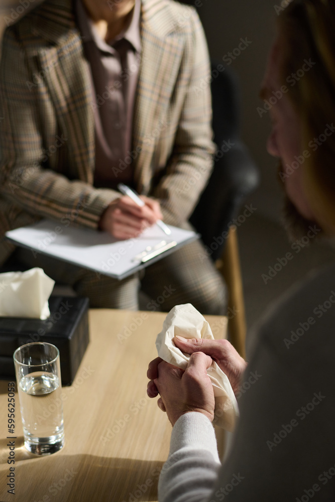 Obraz premium Focus on hands of worried mature man holding paper handkerchief during communication with his psychotherapist during appointment