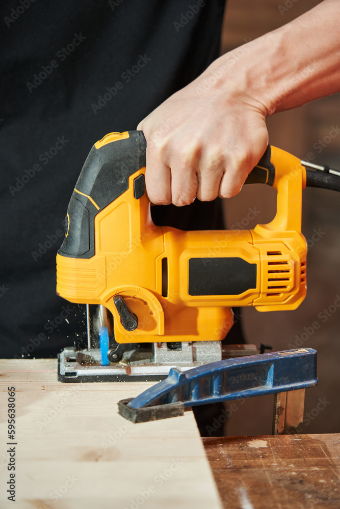 The hand of a Caucasian worker saws a wooden board with an electric jigsaw. chips fly The hand of a Caucasian worker saws a wooden board with an electric jigsaw. chips fly