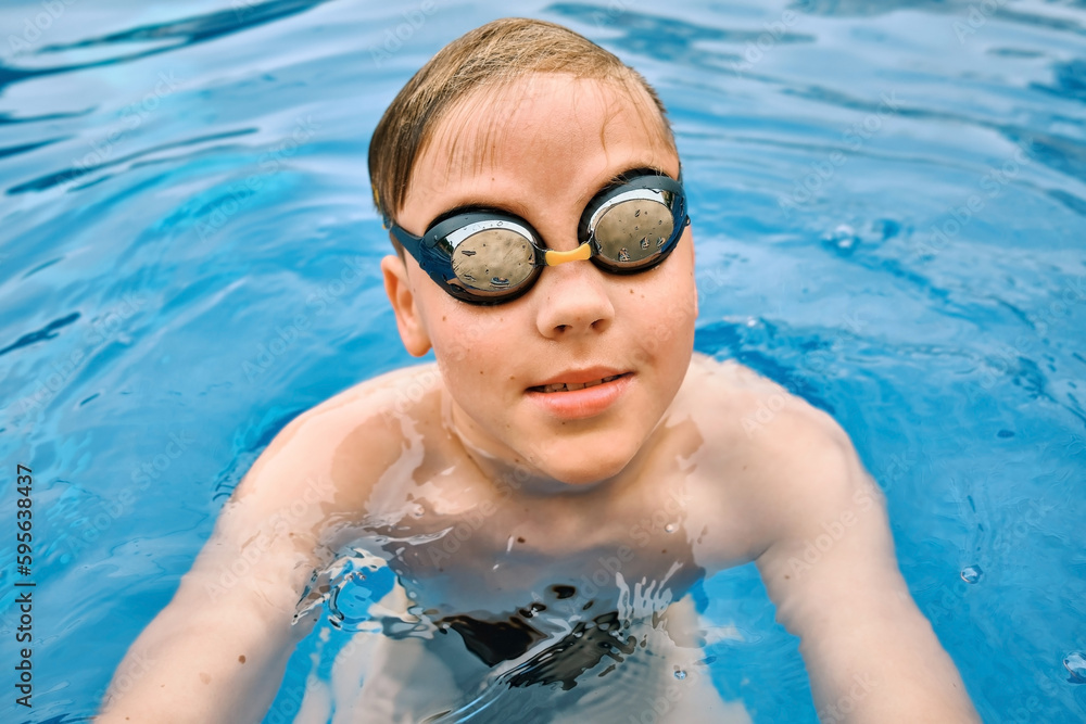 Naklejka premium Smiling boy portrait in swimming goggles, Child swim in the pool, sunbathes, swimming in hot summer day. Relax, Travel, Holidays, Freedom concept.
