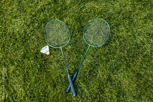 leisure games and sport equipment concept - close up of badminton rackets and shuttlecock on grass