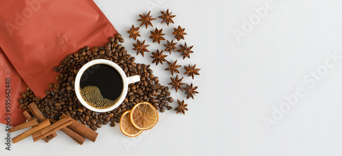 White cup of coffee top view. Coffee beans and packing bag. An invigorating drink in the morning for breakfast. Food background. Copy space banner. Anise stars, cinnamon sticks and dried orange.