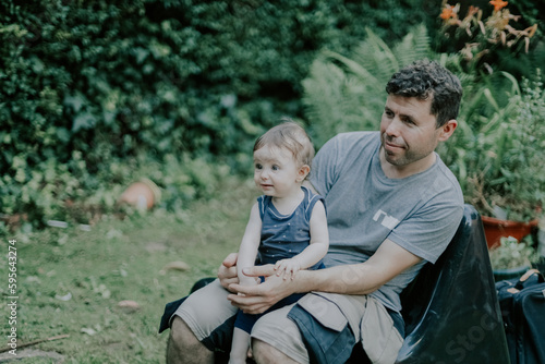 Portrait of a caucasian dad with a baby in his arms and looking away both sitting on a sun lounger © Nataliya