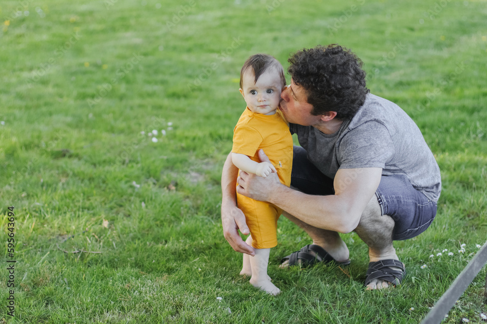 Caucasian young dad holds his little daughter in yellow overalls and reaching out to gently kiss Caucasian young dad holds his little daughter in yellow overalls and reaching out to gently kiss