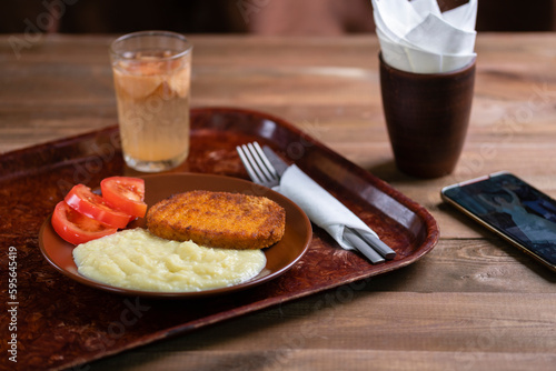 Lunch in the dining room: mashed potatoes with a cutlet and a glass of apple compote on a brown tray