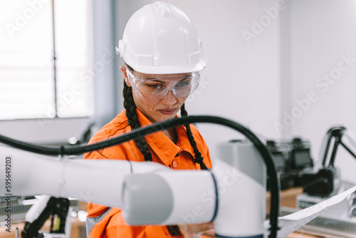 Close up caucasian female automation engineer checking robotic arm welding machine with blueprint, Specialist robot engineers maintenance and testing new innovation for industrial.