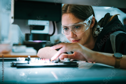 Caucasian female specialist engineer using controller monitor for controlling robotic arm welding machine. Technician maintenance worker in safety uniform working in microchip industry. photo