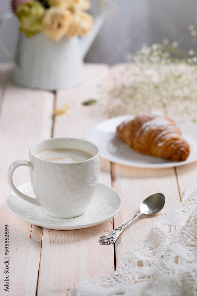 Cappuccino coffee in a white cup with a croissant on a wooden table, high key Cappuccino coffee in a white cup with a croissant on a wooden table, high key