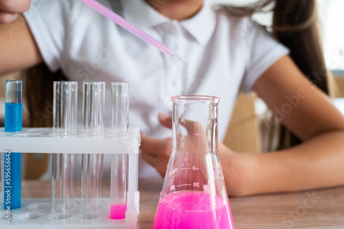 A schoolgirl conducts experiments in a chemistry lesson. Girl pouring colored liquids from a beaker. 