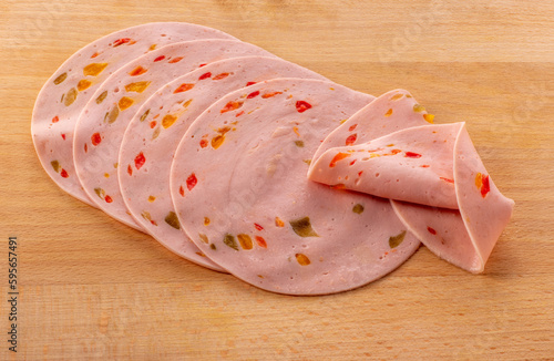 Paprika lyoner sausage slices with red bell pepper, on wooden cutting board