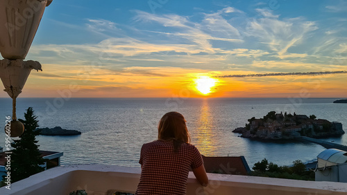 Happy woman on balcony in luxury hotel in Budva Riviera with scenic view on idyllic Sveti Stefan island at sunset, Adriatic Mediterranean Sea, Montenegro, Europe. Summer vacation in seaside resort © Chris