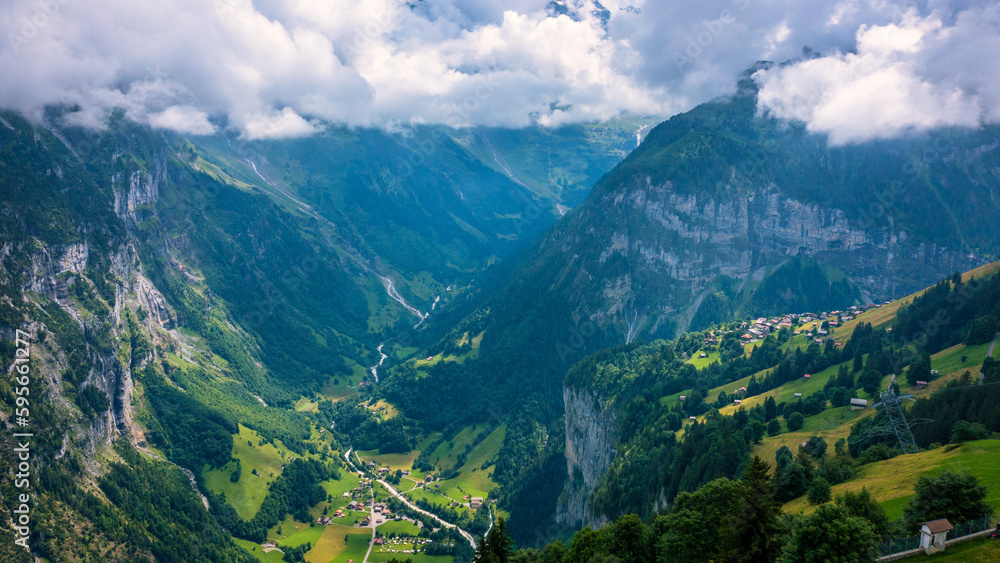 Fototapeta premium Panoramic view of idyllic mountain scenery in the Alps with fresh green meadows in bloom on a beautiful sunny day in summer, Switzerland. Idyllic mountain landscape in the Alps with meadows in summer.