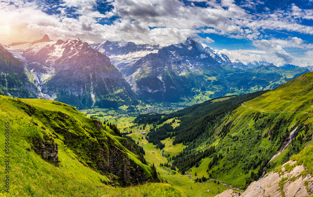 Fototapeta premium Panoramic view of idyllic mountain scenery in the Alps with fresh green meadows in bloom on a beautiful sunny day in summer, Switzerland. Idyllic mountain landscape in the Alps with meadows in summer.
