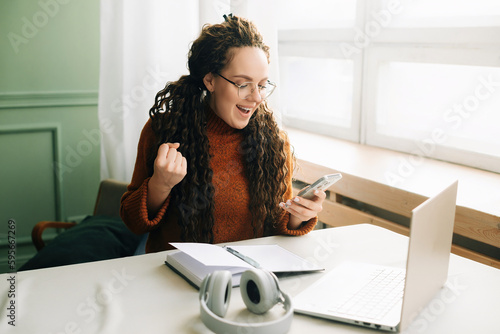 Young happy lucky woman student feeling excited winner holding cellphone using mobile phone winning online, receiving great news or sms offers on a smartphone, getting a new job celebrating success.