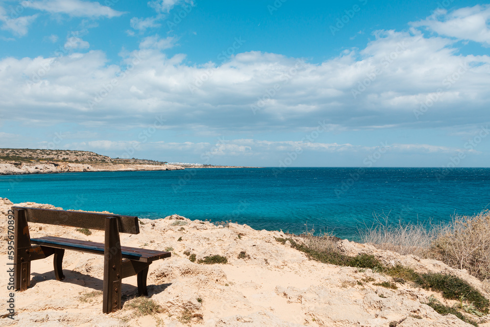 A brown wooden bench on the seashore. View of a beautiful blue lagoon, blue sea water on a sunny day