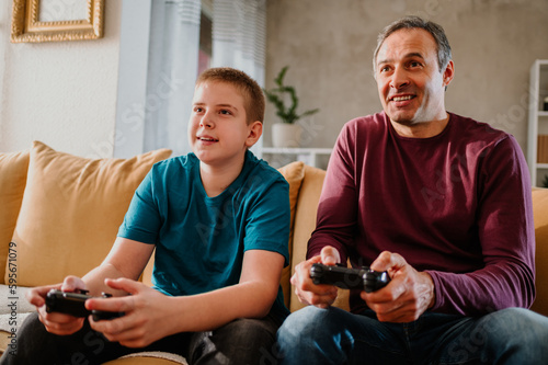 Happy father and his teenage son playing a video game on a free day at home.
