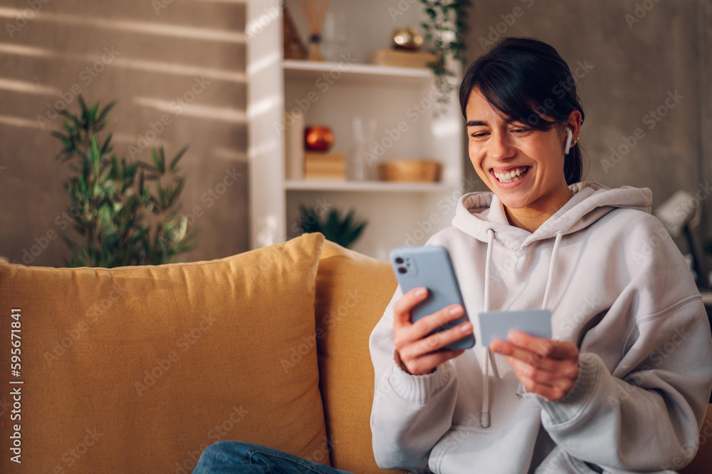 Woman using smartphone and holding credit card while online shopping from home Woman using smartphone and holding credit card while online shopping from home
