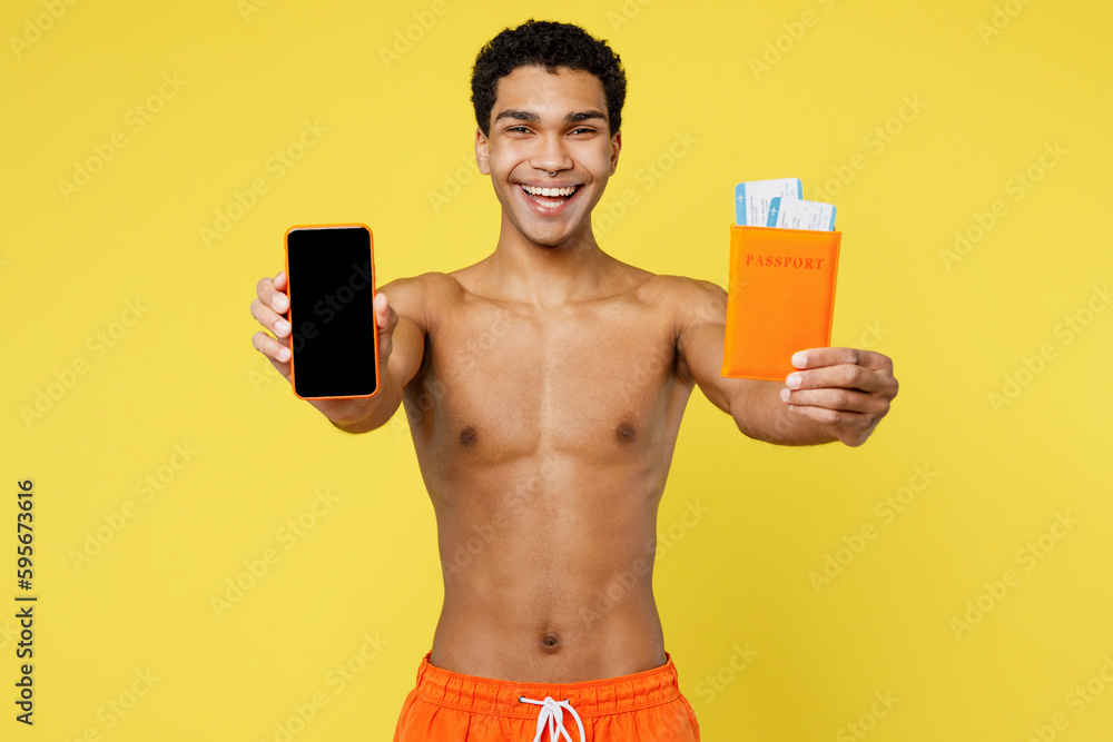 Fototapeta premium Traveler man wear orange shorts swimsuit hold passport ticket use show mobile cell phone isolated on plain yellow background. Tourist travel abroad in free time rest getaway. Air flight trip concept.