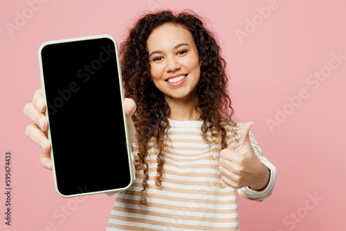 Young woman of African American ethnicity wear light casual clothes hold in hand use close up mobile cell phone with blank screen workspace area show thumb up isolated on plain pastel pink background.