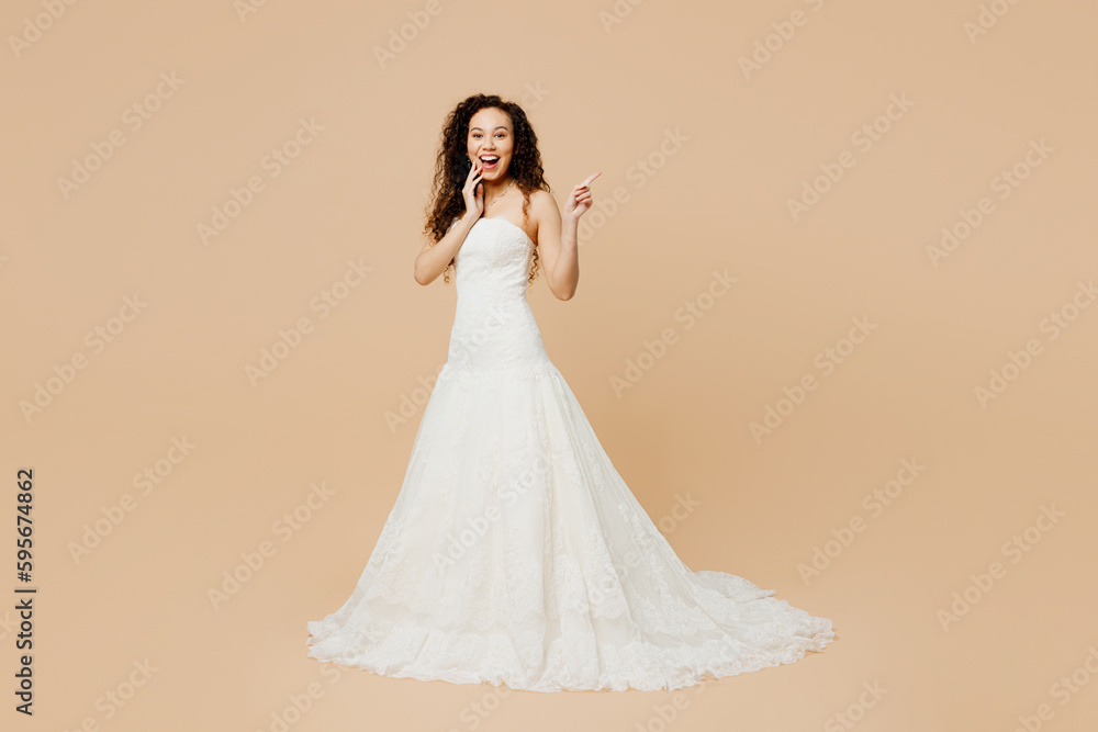 Full body happy smiling young woman bride wear wedding dress posing point index finger aside on area isolated on plain pastel light beige background studio portrait Ceremony celebration party concept