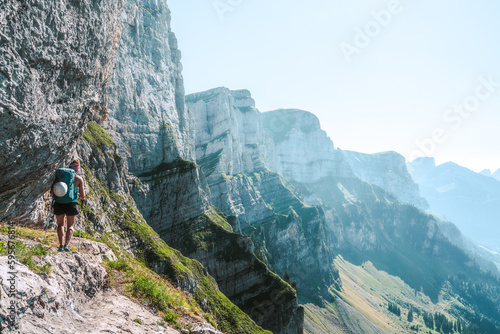 Sporty woman walks on hike trail below steep rock wall with beautiful view on the Churfürsten mountain range. Schnürliweg, Walensee, St. Gallen, Switzerland, Europe.