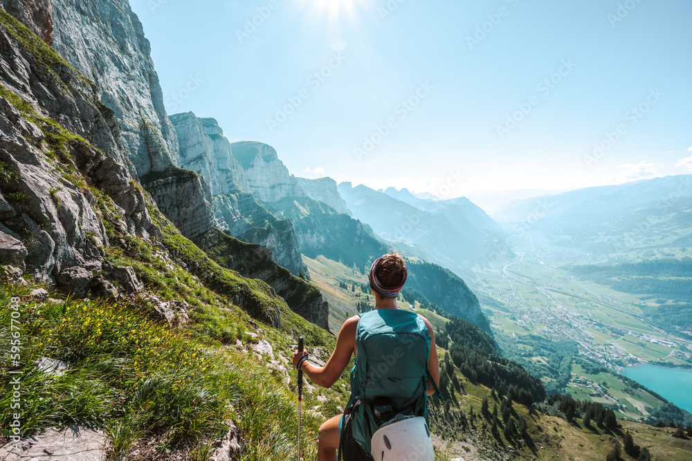 Young woman enjoys scenic view on the Churfürsten mountain range from hike trail below steep rock wall. Schnürliweg, Walensee, St. Gallen, Switzerland, Europe.