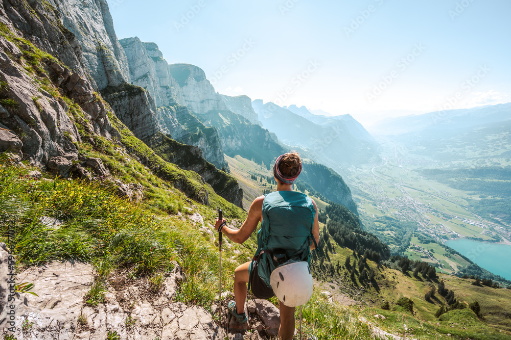 Sporty woman enjoys panoramic view on the Churfürsten mountain range from hike trail below steep rock wall. Schnürliweg, Walensee, St. Gallen, Switzerland, Europe.